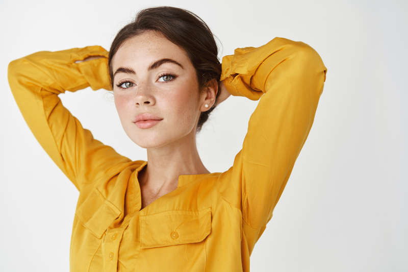 Beautiful woman with stunning eyebrows collecting hair in bun, standing over white background.
