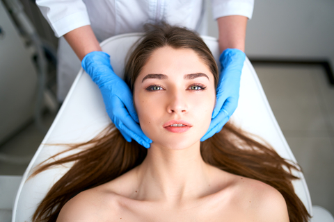 Beautician hands in gloves touching face of attractive woman. Facial Beauty. Beautiful young female with soft smooth healthy skin