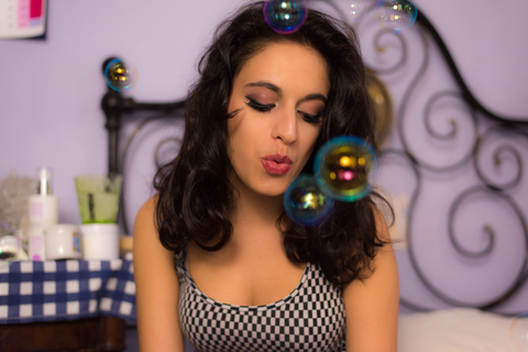 Close up of a beautiful girl with professional make-up. A close up shot a beautiful young girl with red lipstick and a professional make up in incandescent lighting playing with colorful soap bubbles in her messy room.