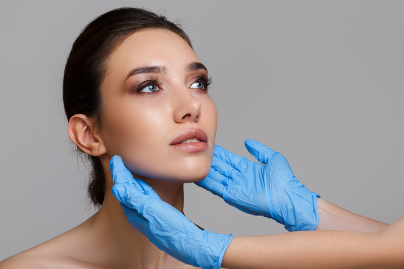 Facial beauty. Portrait of a beautiful young woman with perfect makeup and soft smooth skin. Close-up of beautician hands in gloves touching the face.